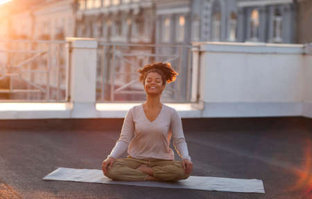 Cropped photo of woman sitting in lotus pose on mat and practicing yoga, female doing namaste gesture while meditating outdoors. meditation and mindfulness conceptの写真素材