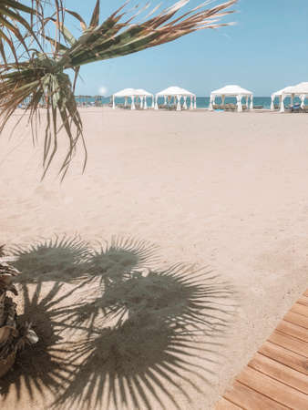 Sandy beach with row of white tents canopies and sun loungers on sunny day at tropical resort, azure sea and clear blue sky on background. travel and vacation conceptの写真素材