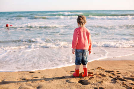 Cute smiling little girl running on sunny beach, happy little girl, enjoying spending time on summer seaside. rear viewの写真素材
