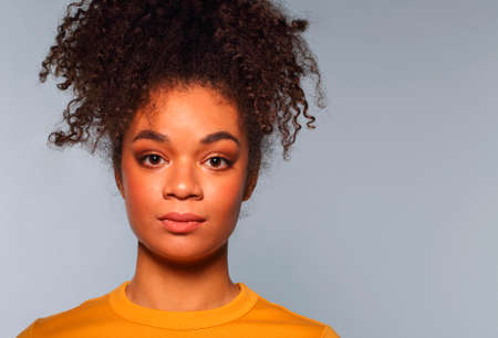 Portrait of ethnic young woman of african race with focused calm facial expression posing on gray studio background, serious focused afro female with curly hair looking straight into cameraの写真素材