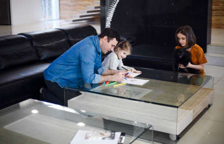 Young man drawing together with little daughters in living room. father spending time with his kids