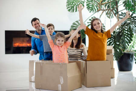 Happy family sitting on the floor in the living room. Funny kids jumping out of cardboard box,...