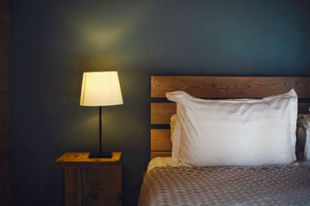 Night scene in cozy room, nightstand with lamp. Bedroom lamp on the night table next to the sleeping bedの写真素材