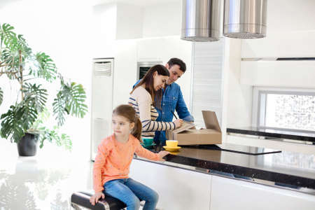 Young happy smiling family three persons unwrapping cardboard cardboard boxes with stuff in light kitchen living room, moving to new flatの写真素材