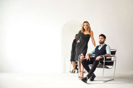 Stylish young ethnic couple embracing against dark gray wall background looking to camera...
