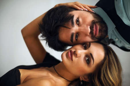 Stylish young ethnic couple embracing against dark gray wall background looking to camera thoughtfully. portrait of the coupleの写真素材