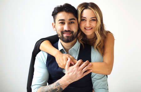Stylish young ethnic couple embracing against light wall background looking to camera with the smile. portrait of the coupleの写真素材