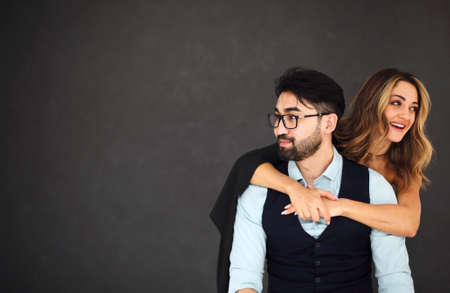 Stylish young ethnic couple embracing against dark gray wall background looking away smiling. portrait of the coupleの写真素材