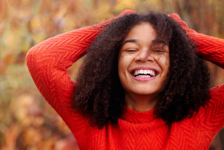 Young happy overjoyed african american woman with curly hair keeping eyes closed laughing and having...