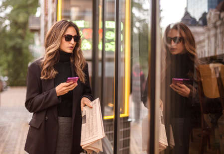 Young elegant fashionable woman wearing black eyeglasses walking on city street and looking in shop...