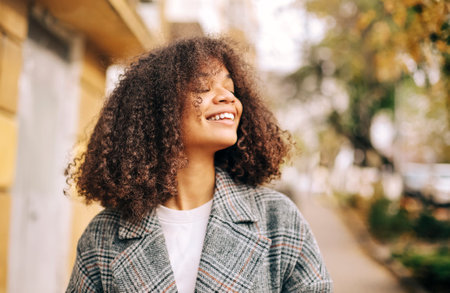 Cute autumn close up portrait of young smiling happy african american woman with curly hair enjoying walk in park in fall season. Outdoor photo of pleased black girl with eyes in love with lifeの写真素材