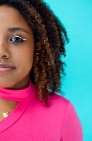 Dreamy young beautiful African American woman with bright eyeline wearing pink bodysuit over blue...