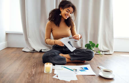 Young brunette african american woman creating her Feng Shui wish map using scissors. Dreams and...