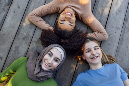 Multiracial young teen female friends resting in the park after sport training laughing and having fun together. Diversity, sport and friendship conceptの写真素材