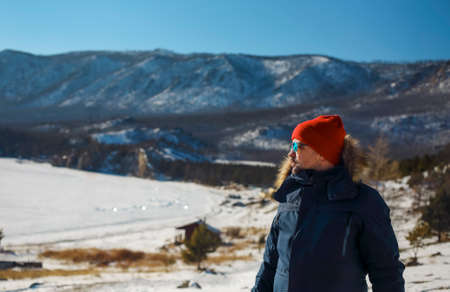 Traveler man in a blue winter jacket ad red cap in the woods. Sandy bay, Baikal lake, winter time. Travel and adventure conceptの写真素材