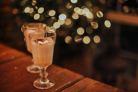 Traditional fall and winter cocktails, alcohol or not. Two glasses of eggnog cocktails with cacao and marshmallows, in two mugs, on wooden table, copy spaceの写真素材