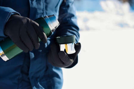 Crop person in blue winter coat and warm glove holding metal cup.の写真素材