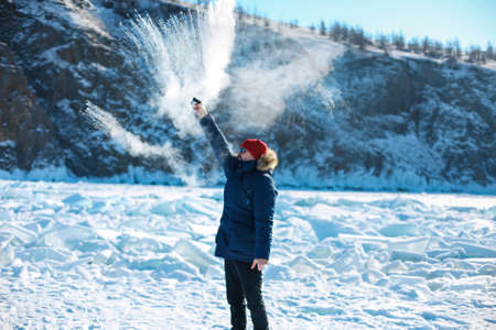 Man in blue jacket pours boiling water that turns into a halo a ball over her head in the form of...