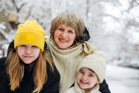 Joyful family grandmother with grandchildren in warm clothes playing outdoors in winter park, enjoying frosty and snowy weather, children actively spending new year holidays in fresh air with grandmaの写真素材