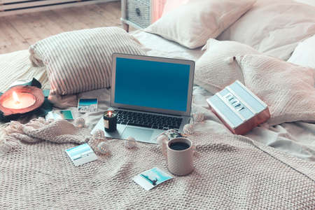 From above various instant photos from summer vacation and mug of hot beverage placed on soft bed near laptop with blue screen at homeの写真素材