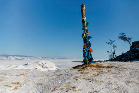 Lake Baikal in winter. Beautiful rocky island on a background of blue sky and ice. Traditional buryat shaman sacred pillar with colorful ribbons in winter, cape Burkhan, Olkhon island. Winter Baikal.の写真素材