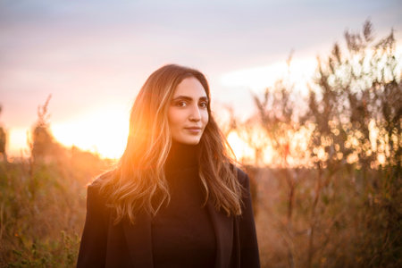 Young happy caucasian brunette woman walking through grassy meadow at sunset and smiling, dreamy beautiful female in evening sunlight standing in autumn field in countrysideの写真素材