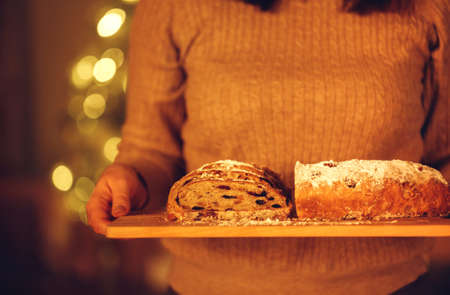 Cropped shot of woman holding delicious freshly baked homemade Christmas pie while standing against blurred xmas tree in background, preparing food for New Years Eve, selective focus on cake in hands. Stollenの写真素材