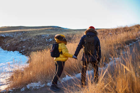 Romantic couple of tourists dressed in warm winter sportswear with tourist backpacks walking in the snowy mountains in an incredible sunset. Ogoi island, Baikal lake. family rest.の写真素材