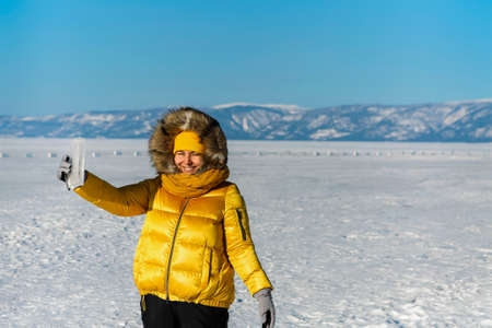 Happy smiling woman wearing winter yellow jacket holding piece of transparent crushed ice cubes over...