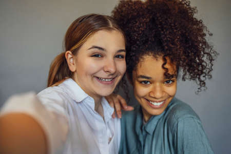 Self-portrait of two happy joyful teen girls of different races smiling at camera, enjoying friendship, multi-ethnic best female friends making selfie photo and having fun while spending time togetherの写真素材