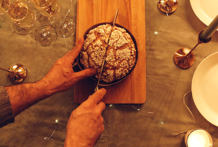 View from above of man cutting delicious freshly baked homemade pie cake with knife on rustic table while preparing cooking Christmas dinner at home. Top view of male hand cuts panettone xmas cakeの写真素材