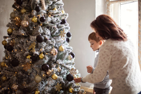 Little preschool boy helping grandmother to decorate Christmas tree at home, grandmom and small grandson decorating xmas firtree together, young family parent and child preparing for New Year celebrationの写真素材