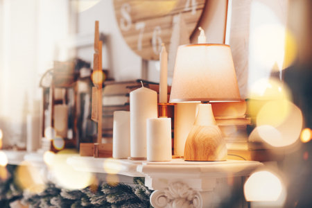 Lamp and many candles on fireplace mantel in house decorated for Christmas holidays, selective focus. Warm details in home interior. Rustic living room with cozy and pleasant atmosphereの写真素材
