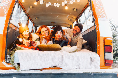 Happy family of travelers in minivan lying together at open rear doors and smiling at camera. Joyful group of people traveling winter snowy nature, spending New Year and Xmas holidays outdoorsの写真素材