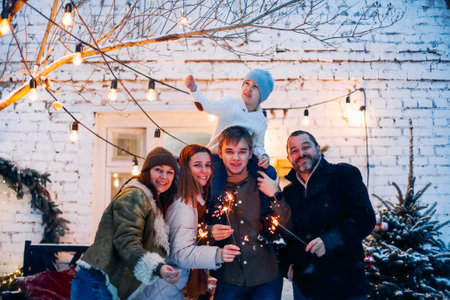 Portrait of big happy family with child standing in snow-covered house yard holding lit sparklers in hands. Parents and children of different age rejoicing Christmas and New Year holidays outdoorsの写真素材