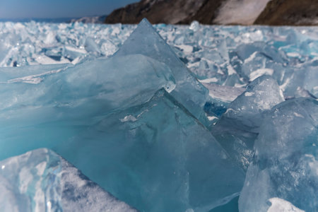 Pieces of ice lying on the ideal smooth ice of baikal with ice hummocks in the horizon. Sun is...