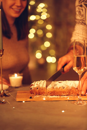 Selective focus of female cutting delicious freshly baked homemade xms pie with knife, celebrating Christmas Eve or New Year with friends or family at home decorated with led lights, defocused. Stollenの写真素材