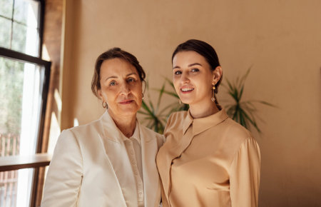 Head shot portrait happy two generations of women hugging, standing at home, smiling mature elderly...