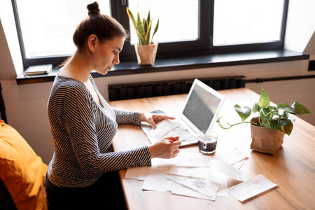 Serious housewife sits at table at home kitchen check household bills, make calculations on...