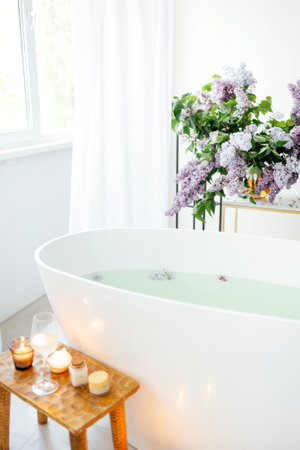 Modern bath room and spa center on the white tub wooden table. Candles and magazine with vases and flowers. White background wall.の写真素材