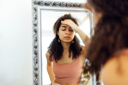 Young unhappy mixed race woman holding her head and suffering from stomach pain and a headache by...