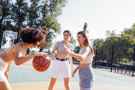 Multicultural group of young female friends bonding outdoors and having fun. Stylish cool teen girls gathering at basketball court, friends playing basketball outdoorsの写真素材