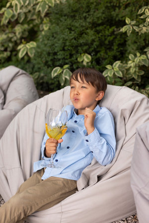 Portrait of little boy drinking juice in a glass, decorated with fruits, with straw at outdoor park. child in summerの写真素材