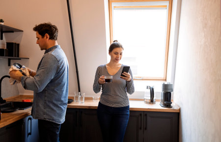 Caring husband helping his wife with dishes In the kitchen. Smiling man cleaning plates while his...