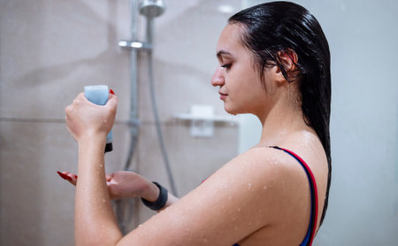 Beautiful smiling young brunette woman taking a shower in the gym. Water drops and bath foam on her...