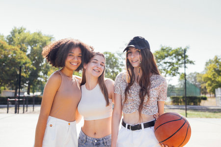 Multicultural group of young female friends bonding outdoors and having fun. Stylish cool teen girls gathering at basketball court, friends ready for playing basketball outdoorsの写真素材