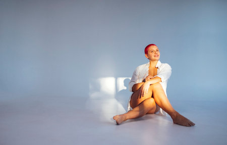 Beautiful relaxed woman in light clothes and red shot hair while resting on sunny weekend day at home. body positive conceptの写真素材