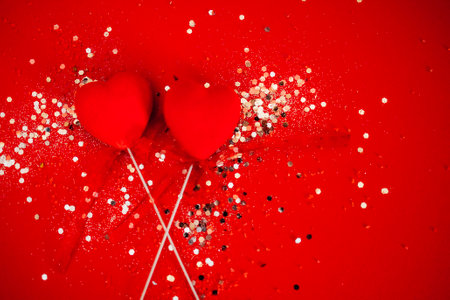 Two decorative hearts on a stick with ribbon. Bright background with silver sequins and round...