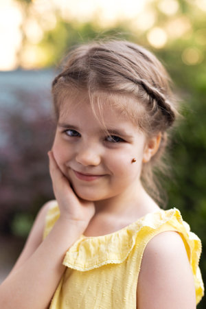 Portrait of the little girl holding hand on one check and have red ladybug on the other one in Summer evening gzrdenの写真素材