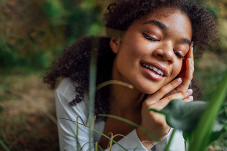 Close up portrait of pretty young african american woman lying on grass. Beautiful afro girl in a...